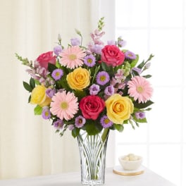 Bouquet of pink, yellow, and purple flowers in a clear glass vase