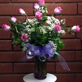 Pink roses in a glass vase with a purple ribbon