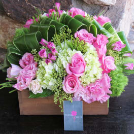 Pink roses and hydrangeas in a wooden box with large green leaves