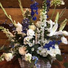 Tall white and blue flower basket with lilies, roses, daisies, hydrangeas, and delphinium in a white woven basket