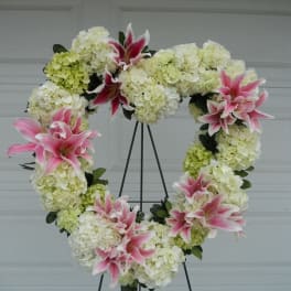 Heart-shaped floral wreath with pink lilies and white hydrangeas on a stand