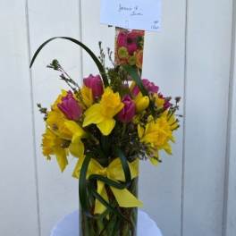 Yellow and pink tulips arranged in a clear glass vase with a yellow ribbon