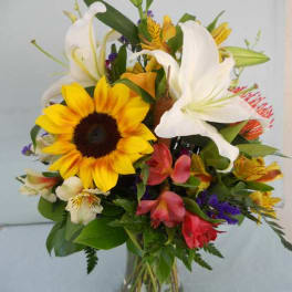 Mixed bouquet with sunflowers, white lilies, and colorful blooms in a glass vase