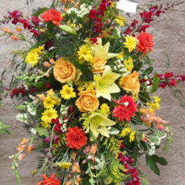 Tall standing spray of mixed flowers in yellow, orange, red, and white