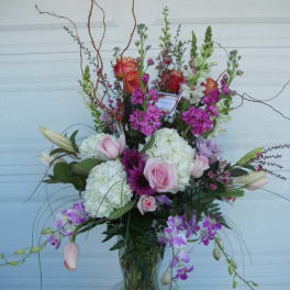 Tall mixed floral arrangement in a glass vase with pink and purple blooms