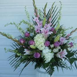 Tall floral arrangement with pink lilies, purple roses, and white hydrangeas in a white vase.