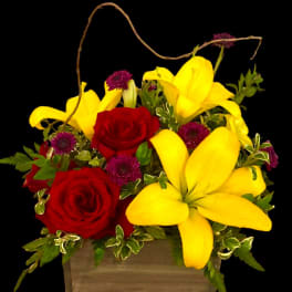 Red roses and yellow lilies in a wooden basket with purple accents