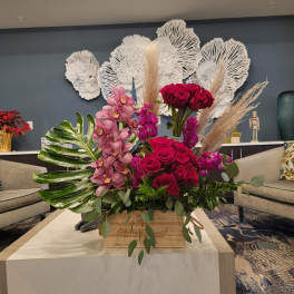 Large arrangement of red roses, pink orchids, and pampas grass in a wooden box