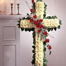 Tall standing cross of white flowers with red roses on a metal easel