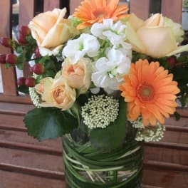 Bouquet of peach roses, orange gerbera daisies, and white flowers in a glass vase