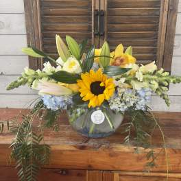 Yellow sunflower and lilies arranged in a glass bowl vase