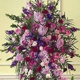 Tall standing spray of pink, purple, and lavender flowers arranged in an elongated oval