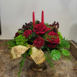 Low red and green holiday centerpiece with roses, candles, pinecones and a gold bow in a pedestal bowl