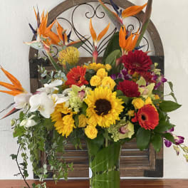 Tropical bouquet with sunflowers, orchids, and bright orange bird-of-paradise in a glass vase