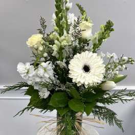 Tall white arrangement with roses, gerbera daisy, snapdragons, and tulips in a clear glass vase tied with raffia.