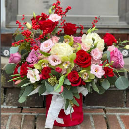 Red and pink rose arrangement in a red box with a white ribbon
