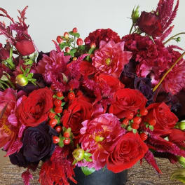 Lush arrangement of red and pink roses and dahlias in a black cylinder vase