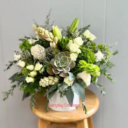 White and green floral arrangement in a white container with a succulent center