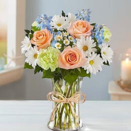 Bouquet of peach roses, white daisies, and blue flowers in a glass vase