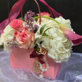 Pink roses and white hydrangeas in a pink gift basket with a ribbon handle