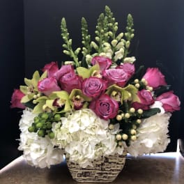 Pink roses and green orchids arranged with white hydrangeas in a patterned vase