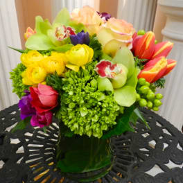 Colorful mixed bouquet in a dark glass vase with tulips, roses, and orchids