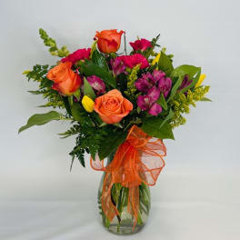 Bouquet of orange roses and pink flowers in a glass vase with an orange ribbon