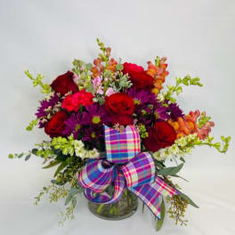Bouquet of red roses, purple daisies, and orange snapdragons in a glass vase with a plaid bow