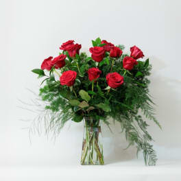 Red roses arranged in a clear glass vase with airy greenery