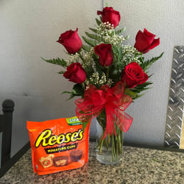 Red roses in a clear vase with a red bow beside a Reese's candy bag