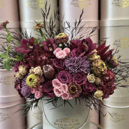 A burgundy and pink floral arrangement in a round hatbox.