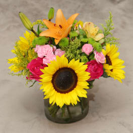 Mixed bouquet with sunflowers, lilies, roses, and carnations in a glass vase