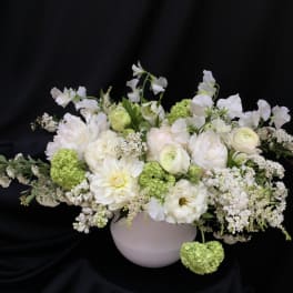 White floral arrangement in a round vase with green accents