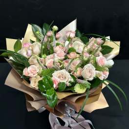 Bouquet of pale pink and white roses wrapped in tan paper