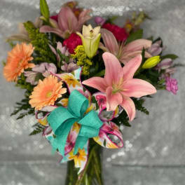 Mixed bouquet of pink lilies and peach daisies in a glass vase with a turquoise bow