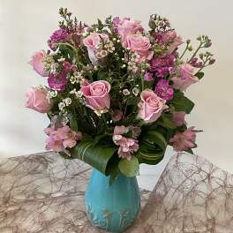 Pink roses and small purple flowers arranged in a turquoise vase