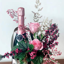 Pink roses arranged around a champagne bottle with pink filler flowers