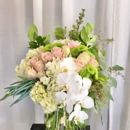 Bouquet of pink roses, white orchids, and green mums in a glass vase