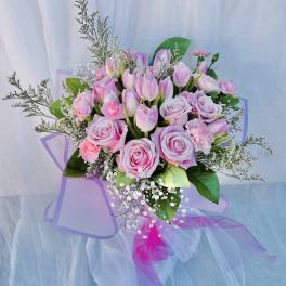Pink roses and tulips arranged with baby's breath in a wrapped bouquet