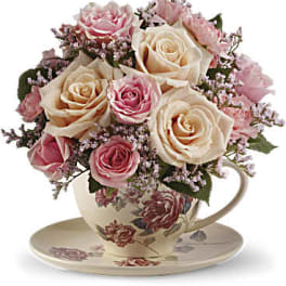 Pink and cream roses arranged in a floral teacup with saucer