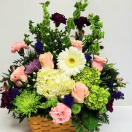 Basket arrangement of pink roses, white gerbera, hydrangea, and purple flowers