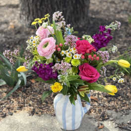 Colorful bouquet of pink roses, ranunculus, and yellow tulips in a striped ceramic pitcher.