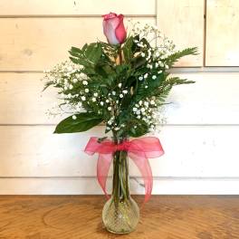 Single pink rose in a glass vase with baby's breath and a pink ribbon