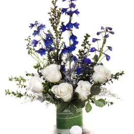 White roses and blue flowers arranged in a green glass vase