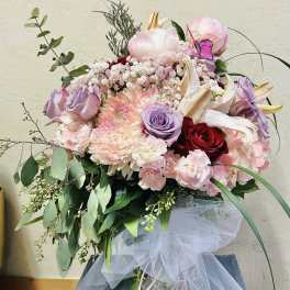 Bouquet of pink, lavender, and red flowers with white lilies and tulle ribbon