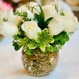 White roses arranged in a clear glass vase with green foliage