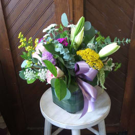 Mixed bouquet with lilies, roses, and a purple ribbon in a vase