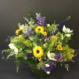 Low mixed arrangement of yellow and purple flowers in a round clear glass vase
