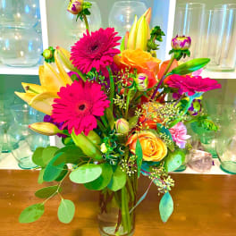 Bright mixed bouquet of gerbera daisies, roses, and lilies in a glass vase