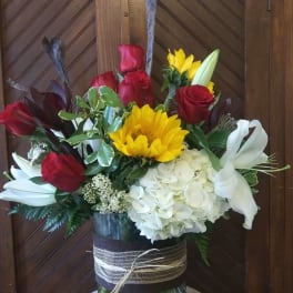 Tall bouquet of red roses, white lilies, yellow sunflower, and white hydrangea in a glass vase